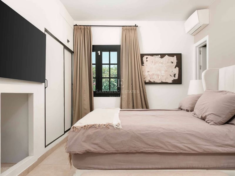 Chambre lumineuse avec lit mauve, TV murale, rangements intégrés et fenêtre avec rideaux taupe.
