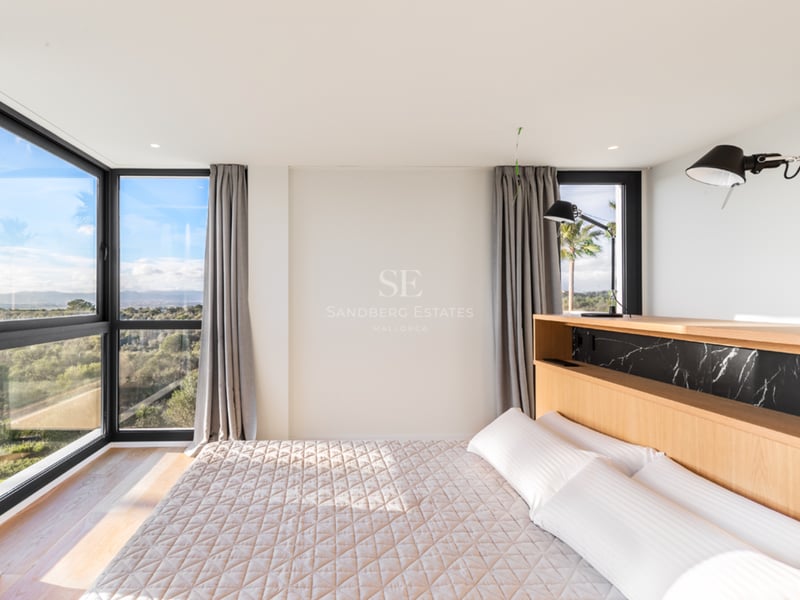 Chambre lumineuse avec tête de lit en chêne, accents de marbre noir et grandes fenêtres d'angle donnant sur la nature.