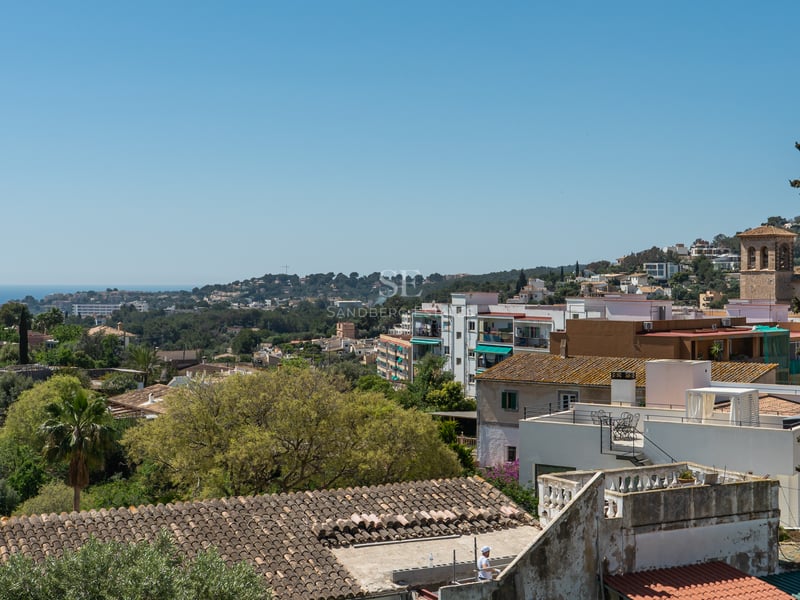 Vue sur les toits méditerranéens, les collines verdoyantes et la mer bleue au loin sous un ciel clair.