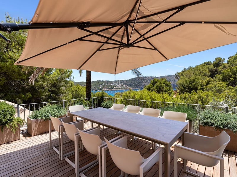 Terrasse extérieure en bois avec table à manger et chaises sous un grand parasol donnant sur la mer.