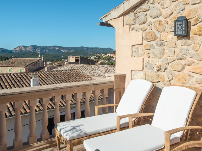 Deux chaises longues blanches sur une terrasse en pierre avec vue sur un village méditerranéen et les montagnes.