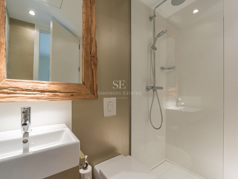 Salle de bain moderne avec douche à l'italienne en verre, lavabo blanc et miroir avec cadre en bois brut.