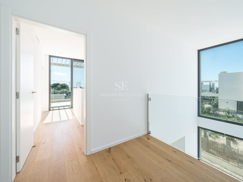 Couloir lumineux avec parquet clair, rampe en verre et grandes fenêtres offrant une vue sur l'extérieur.