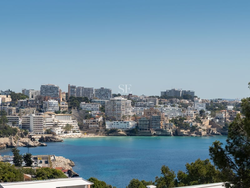 Vue surplombante d'une baie aux eaux turquoise entourée d'une architecture côtière sous un ciel bleu.