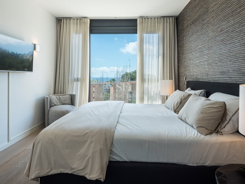 Chambre contemporaine avec grand lit, mur d'accent texturé et fenêtre donnant sur la mer et le ciel bleu.
