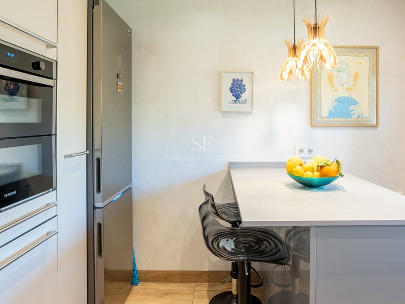 Vue d'une cuisine contemporaine avec double four Samsung, réfrigérateur inox et îlot avec tabourets de bar noirs.