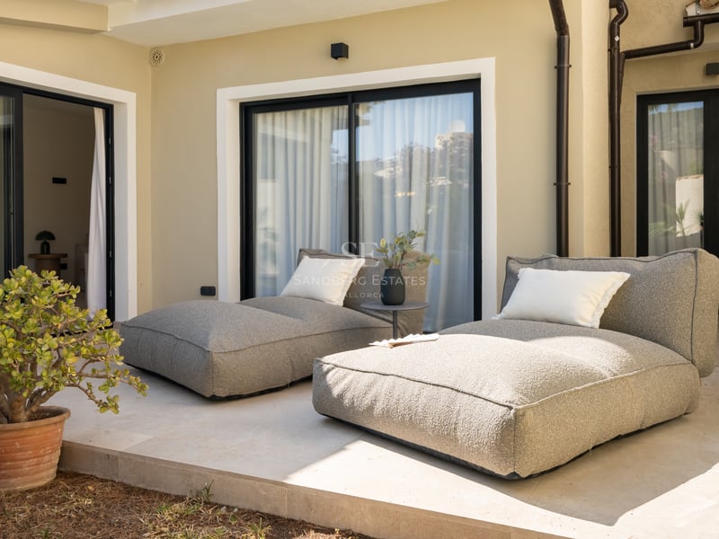 Deux chaises longues en tissu gris sur une terrasse en pierre naturelle devant des baies vitrées et une plante grasse.