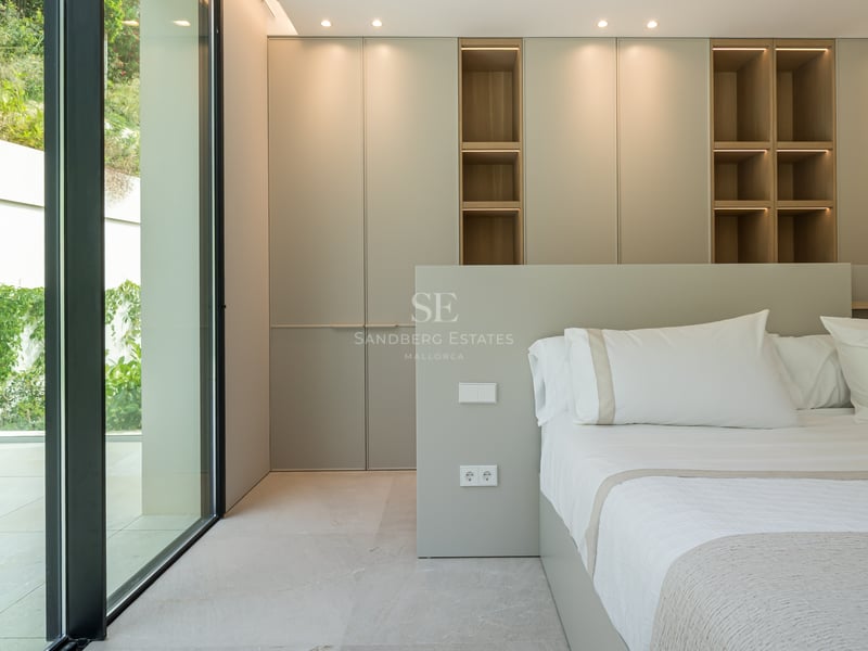Chambre contemporaine avec baies vitrées, placards toute hauteur et étagères en bois avec éclairage LED.
