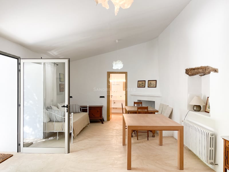 Chambre lumineuse avec lit en métal blanc, table en bois et sol en microciment poli sous un plafond voûté.