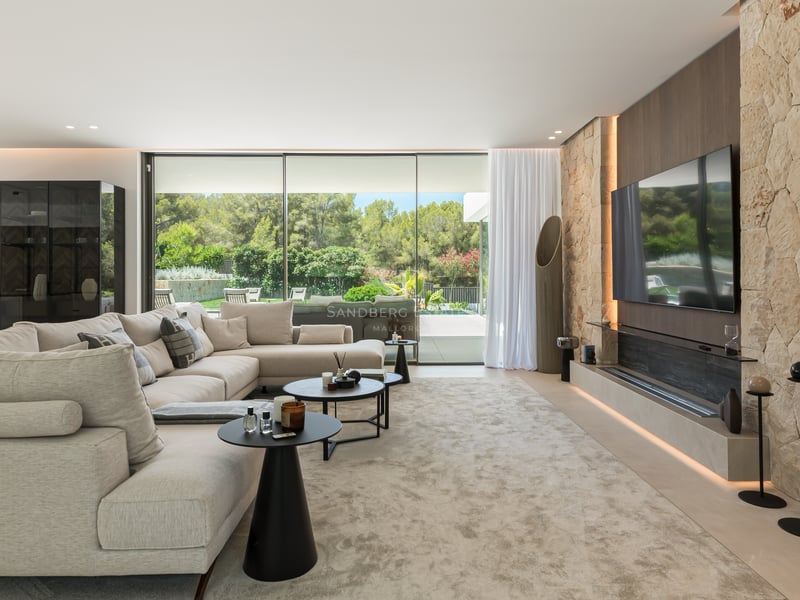 Vaste salon moderne avec mur en pierre naturelle, grand canapé beige et baies vitrées donnant sur le jardin.
