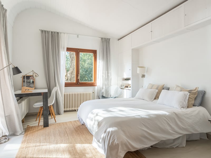 Chambre baignée de lumière avec literie blanche, plafond voûté, tapis en fibres naturelles et bureau d'angle.