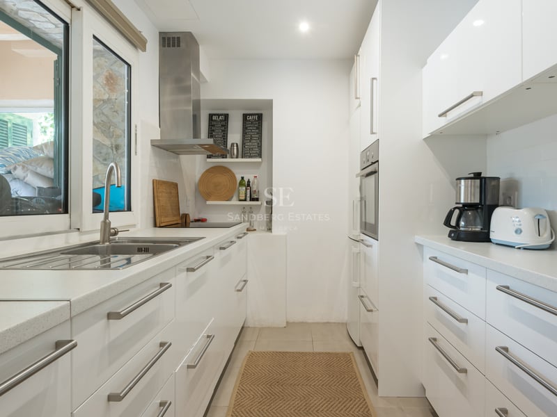 Cuisine lumineuse avec placards blancs brillants, plans de travail en quartz et appareils en inox.
