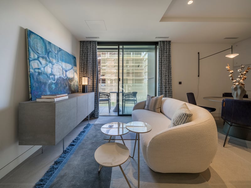 Salon contemporain avec canapé incurvé blanc, buffet en béton et grandes baies vitrées ouvrant sur un balcon.