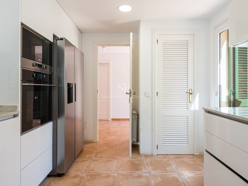 Cuisine lumineuse avec placards blancs, plans de travail en marbre, frigo inox et sol en terre cuite.