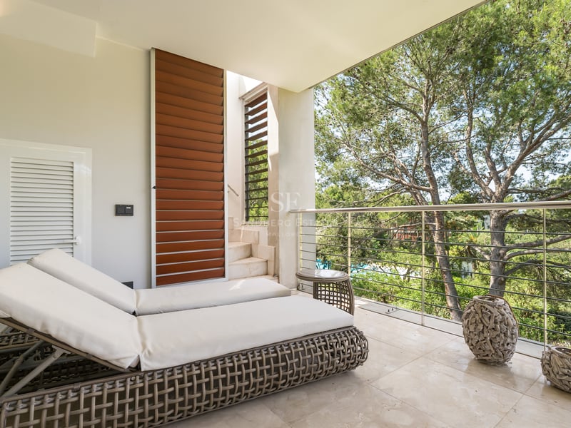 Terrasse moderne avec bains de soleil, sol en marbre et garde-corps en inox donnant sur une pinède.