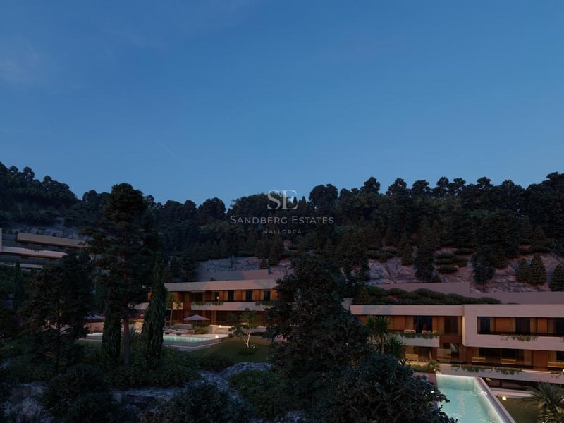 Vue nocturne d'une villa moderne à plusieurs niveaux avec fenêtres éclairées, piscine à débordement et forêt dense.
