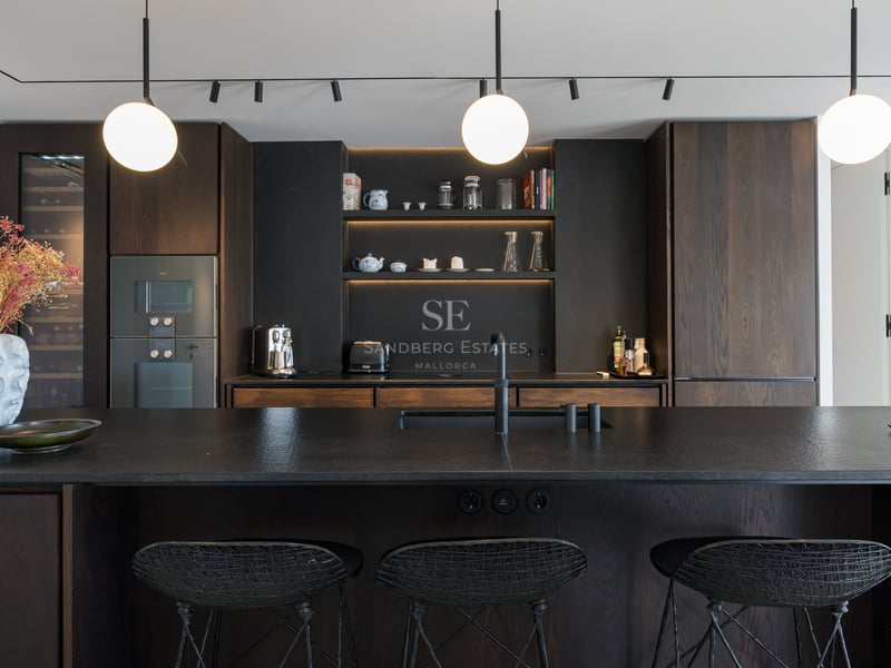 Cuisine moderne avec placards en bois sombre, îlot noir texturé avec tabourets et suspensions sphériques.