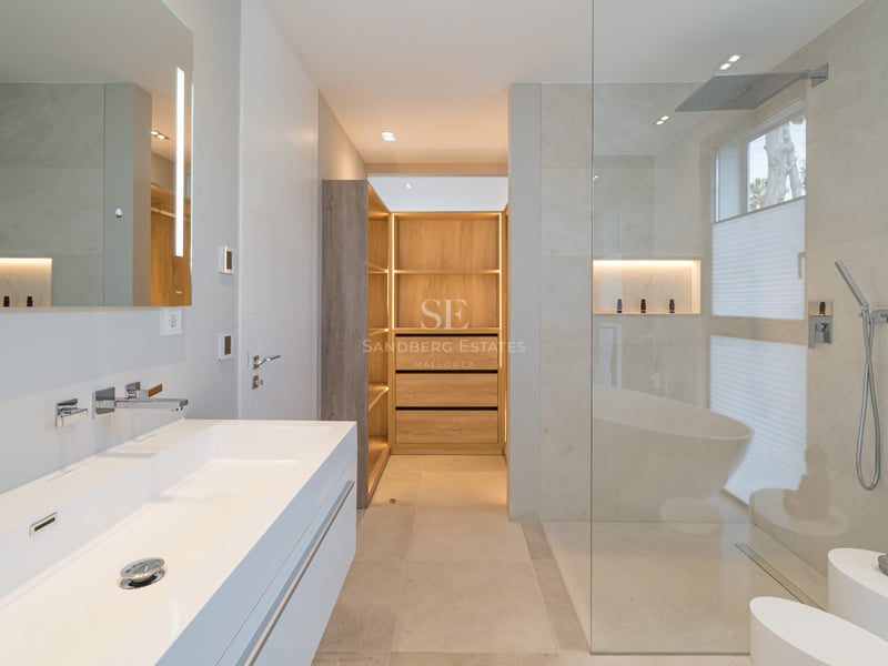 Salle de bains de luxe avec double vasque blanche, douche à l'italienne et dressing en bois éclairé.