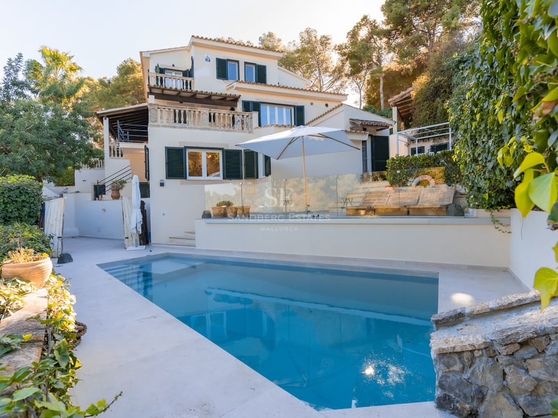 Piscine privée devant une villa blanche de style méditerranéen avec volets verts et environnement boisé.