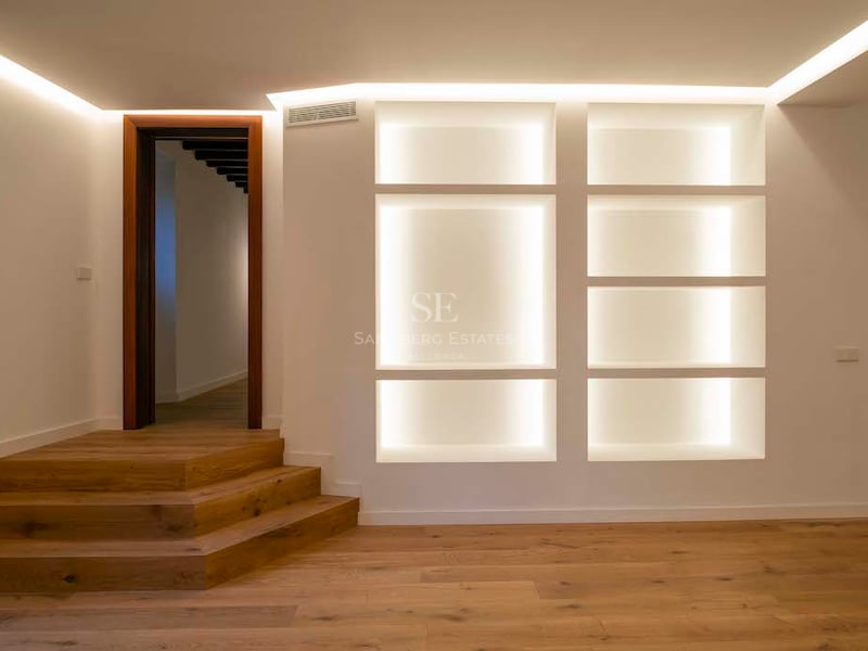 Pièce moderne avec parquet en bois, marches en chêne et étagères encastrées éclairées par des lumières LED chaleureuses.