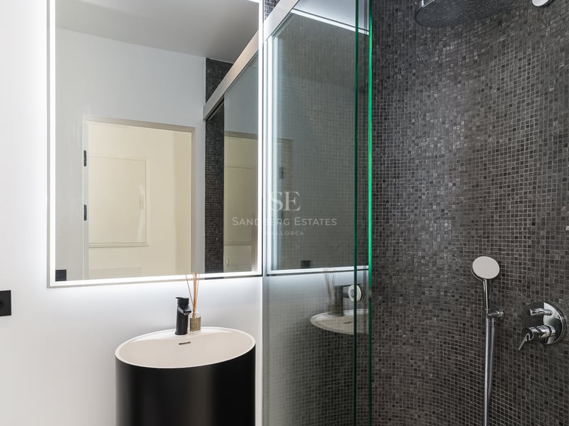 Salle de bain contemporaine avec vasque cylindrique noire, miroir rétroéclairé LED et douche en mosaïque anthracite.
