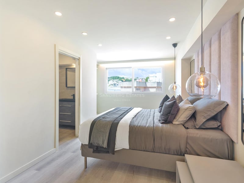 Chambre moderne avec tête de lit en velours rose, suspensions en verre et accès à la salle de bain attenante.