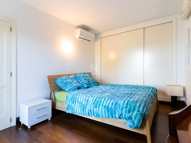 Chambre avec lit en bois, literie bleue, murs blancs, parquet foncé et placard intégré.
