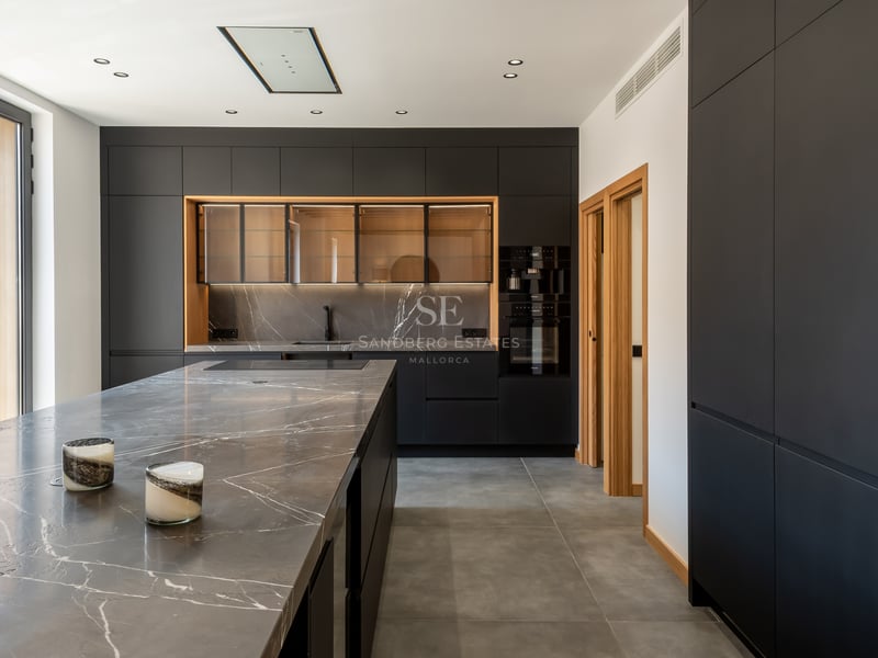 Cuisine moderne avec placards noir mat, plan de travail en marbre gris veiné et grandes fenêtres.