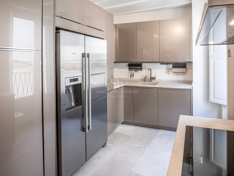 Cuisine moderne avec placards taupe brillant, réfrigérateur en acier inoxydable et plans de travail en pierre claire.