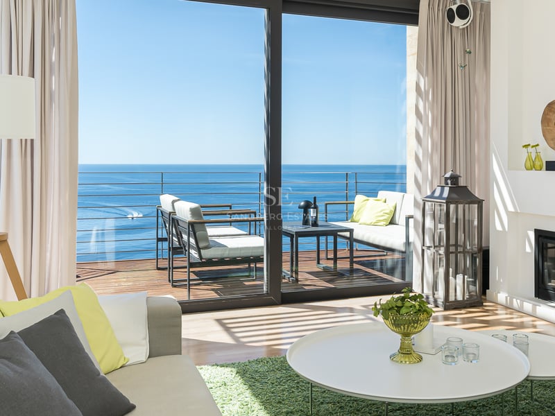 Salon moderne avec cheminée et baies vitrées ouvrant sur une terrasse avec vue directe sur la mer Méditerranée.