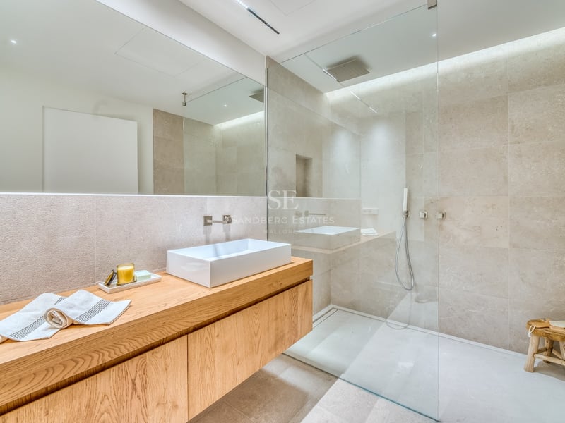 Salle de bain moderne avec meuble en chêne, vasque blanche et douche vitrée aux murs en pierre.