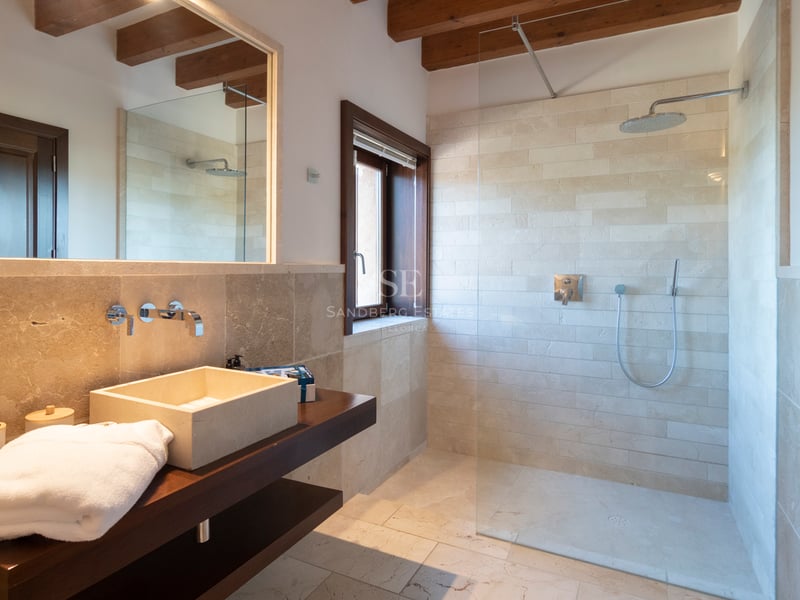 Salle de bain contemporaine avec murs en pierre naturelle, douche à l'italienne et poutres en bois apparentes.