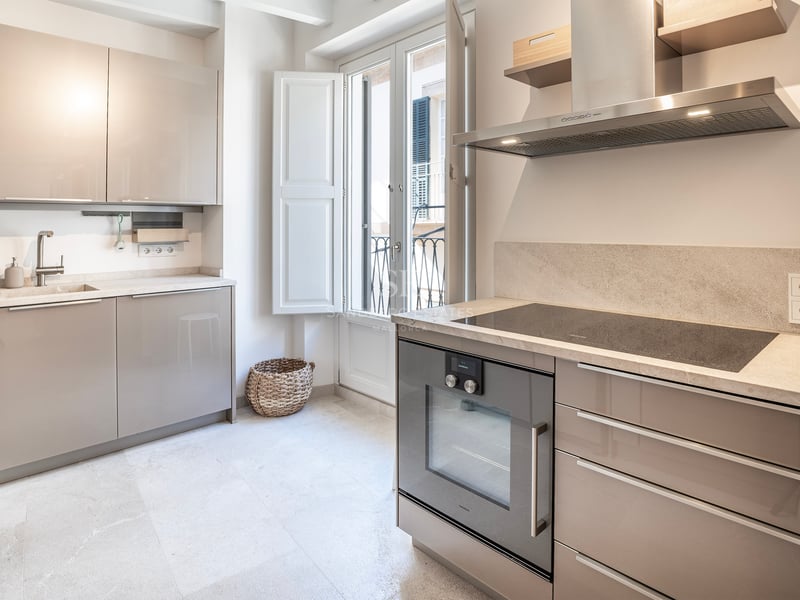 Cuisine moderne lumineuse avec placards beige brillant, plan de travail en pierre et porte-fenêtre.