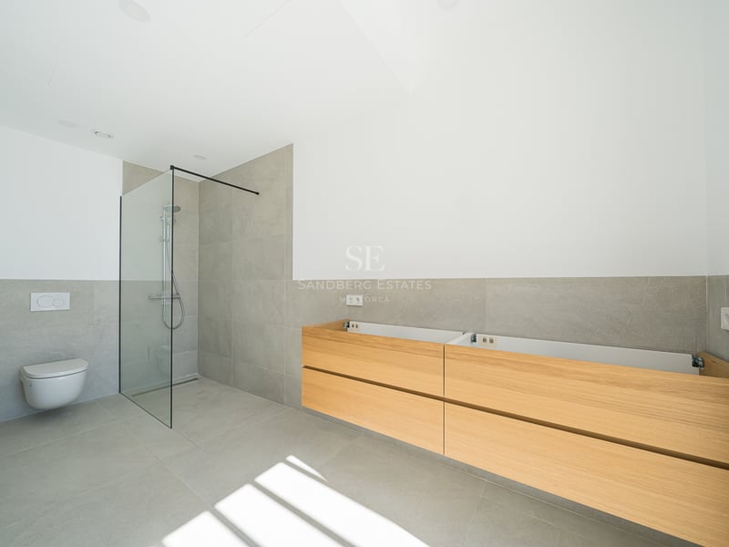 Salle de bain moderne avec carrelage gris, douche à l'italienne en verre, WC suspendu et meuble en bois.