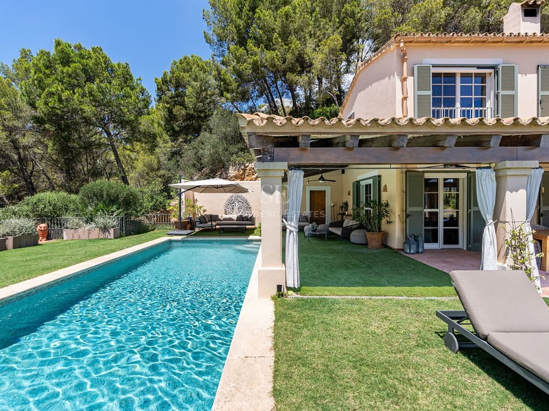 Piscine rectangulaire turquoise à côté d'une villa méditerranéenne avec terrasse couverte et volets verts.
