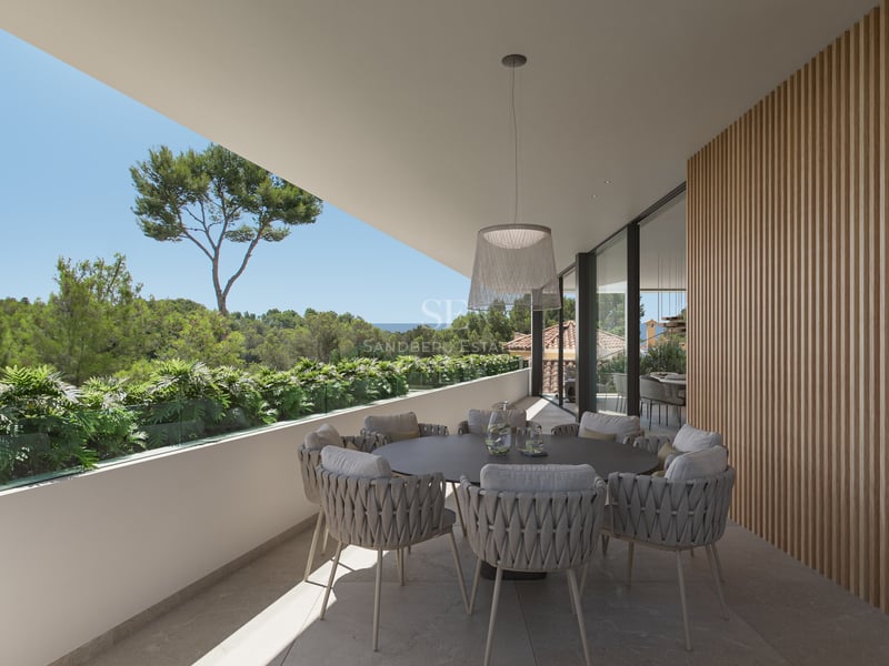 Terrasse moderne avec table ronde, chaises tressées, mur en lattes de bois et vue sur la forêt et la mer.