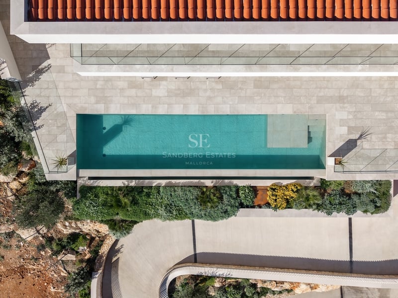 Vue plongeante d'une piscine turquoise, d'une terrasse en pierre, d'un toit en terre cuite et d'un jardin.