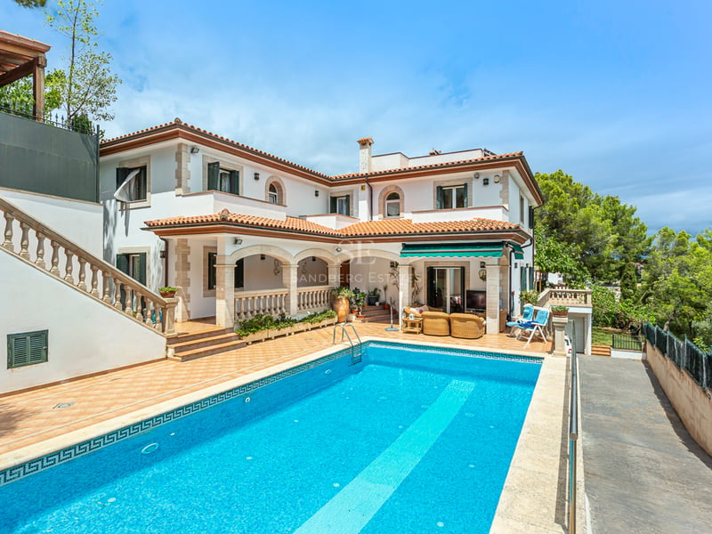 Grande piscine rectangulaire devant une villa méditerranéenne blanche à deux étages avec toit en terre cuite.