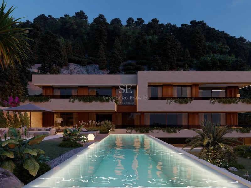 Vue nocturne d'une villa contemporaine avec piscine éclairée et arrière-plan de montagnes boisées.
