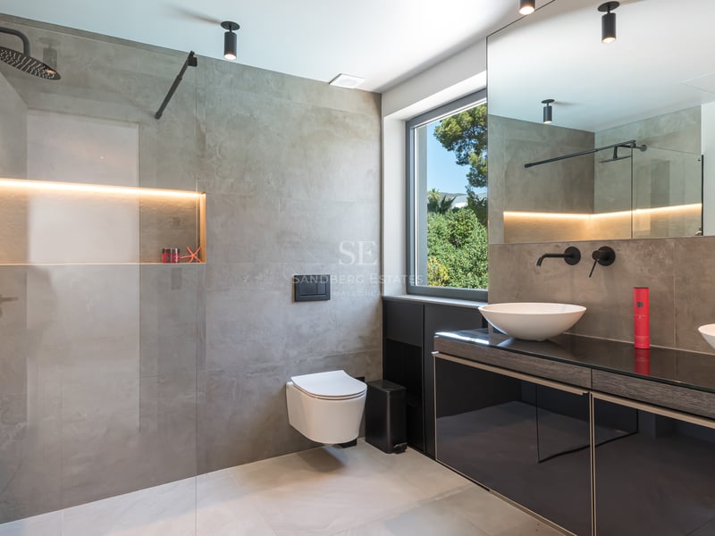 Salle de bains contemporaine avec grands carreaux gris, douche à l'italienne, double vasque et robinetterie noir mat.