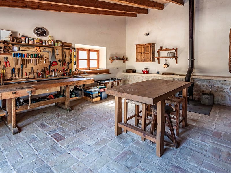 Atelier traditionnel avec un grand établi en bois, des outils au mur et des sols en pierre rustique.