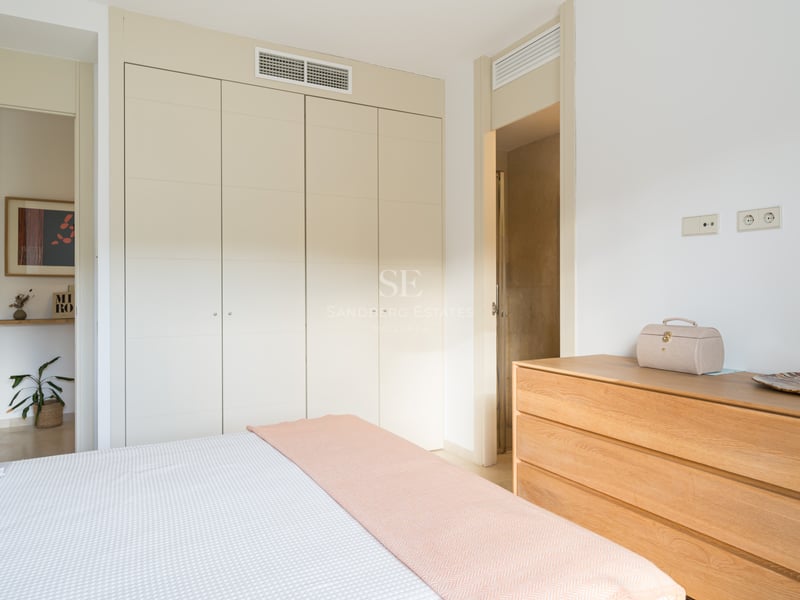 Chambre lumineuse avec placards crème, commode en bois et lit avec jeté de lit rose pastel.