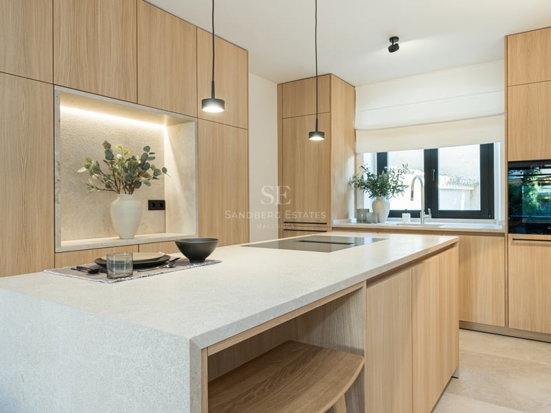 Cuisine moderne avec placards en chêne clair, grand îlot en pierre avec plaque à induction et appareils intégrés.