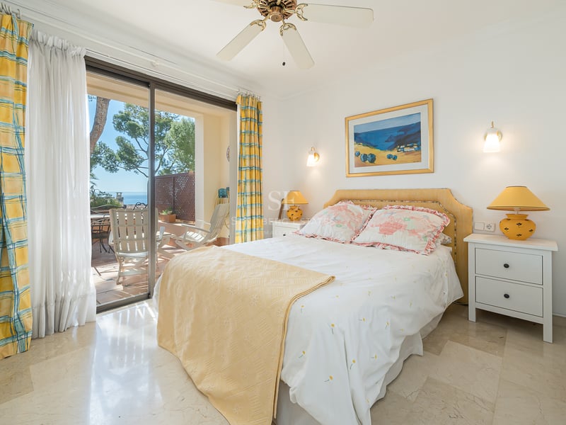 Chambre lumineuse avec sol en marbre, décor jaune et portes coulissantes ouvrant sur une terrasse avec vue sur la mer.