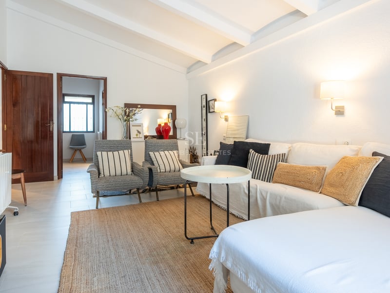 Salon lumineux avec canapé blanc, fauteuils rayés, tapis en jute et poutres de plafond blanches.