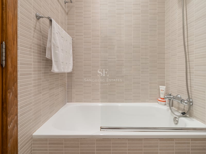 Baignoire blanche encastrée avec paroi vitrée et carrelage beige dans une salle de bain lumineuse.