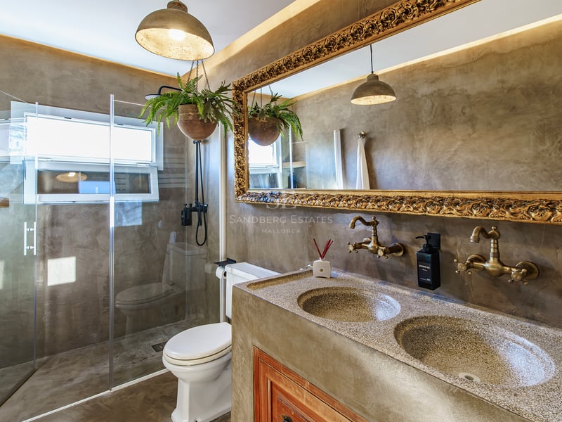 Salle de bain de luxe avec murs en béton, miroir doré orné, double vasque et douche en verre.