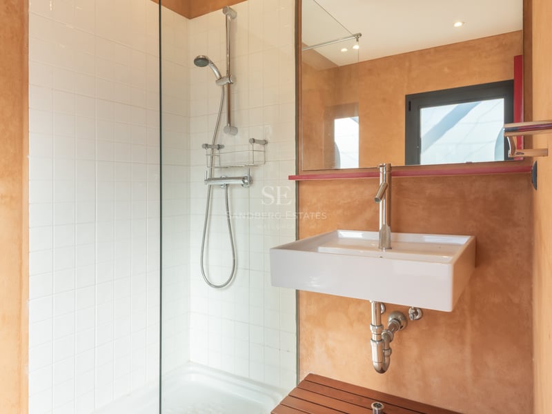 Salle de bain moderne avec douche en verre, carreaux blancs et murs texturés terre cuite avec vasque blanche.