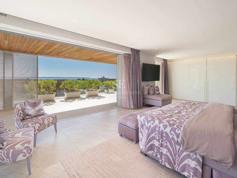 Chambre de luxe avec lit double, accès terrasse en bois et vue sur l'océan à travers de grandes baies vitrées.