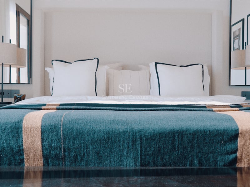 Lit king-size avec jeté de lit bleu canard, lampes design symétriques et miroirs muraux dans une suite de luxe.